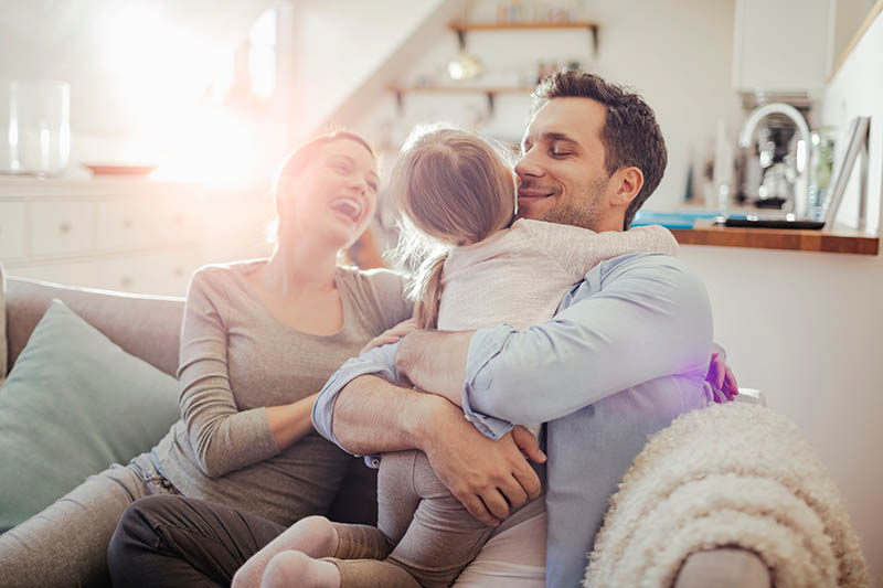 Happy young family relaxing on the couch at home IAQ AirFiltration Supporting 800x533 1