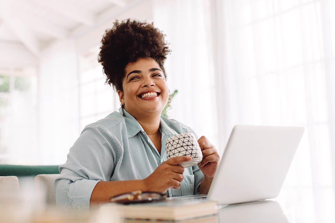 Woman taking break while working from home woman smiling while drinking coffee and working on her laptop