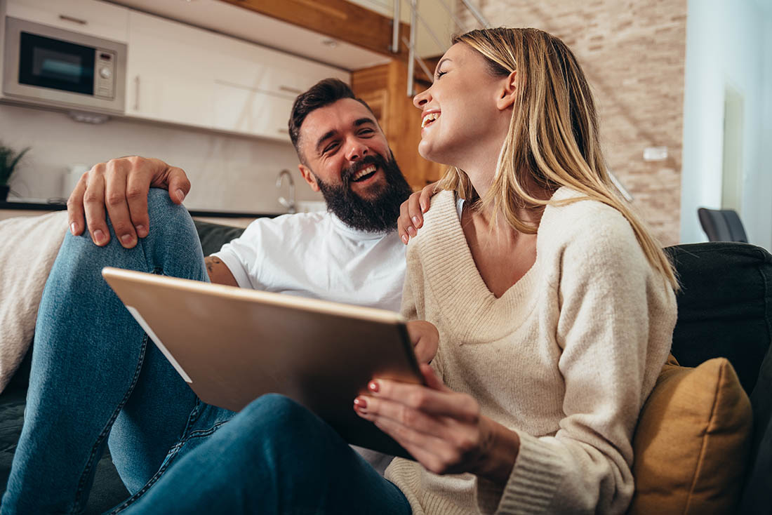Couple using a digital tablet at home Couple sitting with their tablet laughing